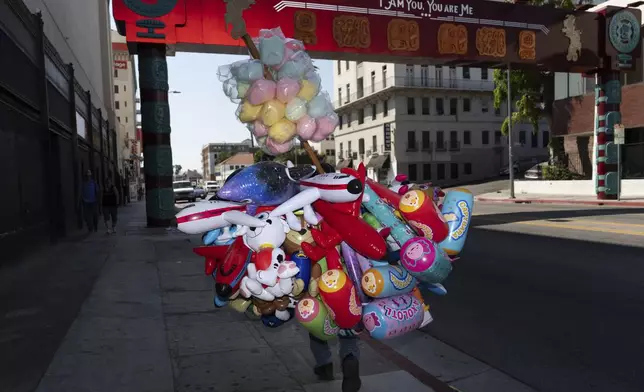 A street vendor carries cotton candy and inflatable toys near MacArthur Park in Los Angeles, an area targeted in recent ICE raids, Saturday, July 19, 2025. (AP Photo/Jae C. Hong)