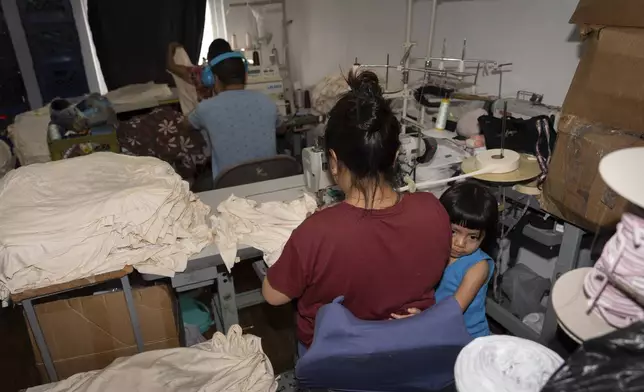 Anaise, 3, clings to her mother, Veronica, an immigrant from Guatemala, as she works at a sewing machine in Los Angeles, Monday, Aug. 4, 2025, amid ongoing ICE raids. (AP Photo/Jae C. Hong)