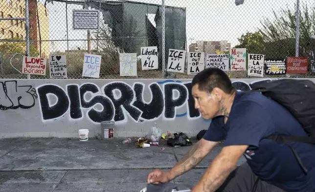 A man rides his bike past signs protesting ICE, displayed on a fence across the street from a Home Depot in Los Angeles, Tuesday, Aug. 5, 2025, amid ongoing ICE raids. (AP Photo/Jae C. Hong)