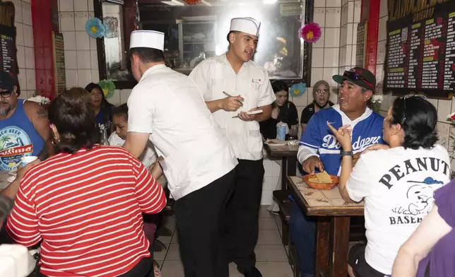 Diego Garcia, center right, who said he worries about his parents amid ICE raids, takes an order from diners at a restaurant on Olvera Street in Los Angeles, Saturday, July 19, 2025. (AP Photo/Jae C. Hong)