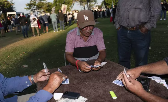 Guillermo Trejo, center, plays cards with friends at a park in Oxnard, Calif., Friday, July 18, 2025, as demonstrators gather to protest a recent ICE raid. (AP Photo/Jae C. Hong)