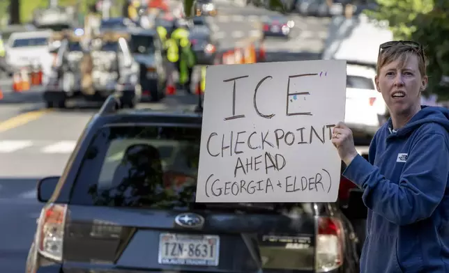 People hold signs warning drivers of a checkpoint operated by the Metropolitan Police Department and federal agencies, including officers from Immigration and Customs Enforcement (ICE) and Homeland Security Investigations (HSI), on Georgia Avenue in the northern part of Washington, Saturday, Aug. 30, 2025. (AP Photo/Mark Schiefelbein)