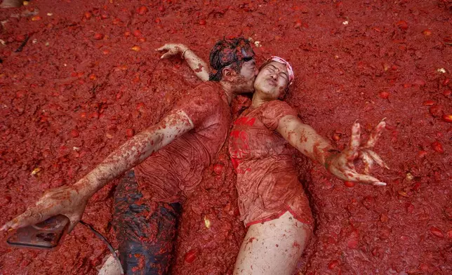A couple kisses over a puddle of tomatoes during the annual "Tomatina" tomato fight fiesta, in the village of Bunol near Valencia, Spain, Wednesday, Aug. 27, 2025. (AP Photo/Alberto Saiz)