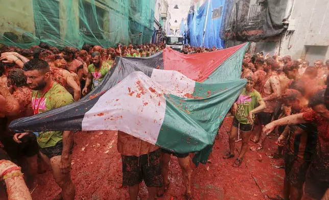 Revelers hold a Palestinian flag as they throw tomatoes at each other during the annual "Tomatina" tomato fight fiesta, in the village of Bunol near Valencia, Spain, Wednesday, Aug. 27, 2025. (AP Photo/Alberto Saiz)
