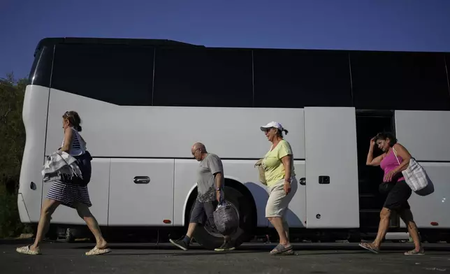 People arrive by bus at Avlaki beach about 42 kilometers (26 miles) east of Athens, Greece, Wednesday, Aug. 19, 2025. (AP Photo/Thanassis Stavrakis)