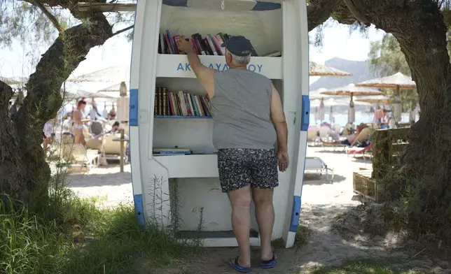 A man borrows a book from a lending library at Avlaki beach about 42 kilometers (26 miles) east of Athens, Greece, Thursday, Aug. 7, 2025. (AP Photo/Thanassis Stavrakis)