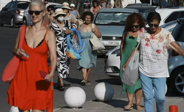 People arrive by bus at Avlaki beach about 42 kilometers (26 miles) east of Athens, Greece, Wednesday, Aug. 19, 2025. (AP Photo/Thanassis Stavrakis)