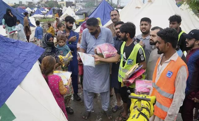 Volunteers distribute clothes among families at a relief camp set up for people who fled their homes following torrential rains and rising water level in the Ravi river, on the outskirts of in Lahore, Pakistan, Sunday, Aug. 31, 2025. (AP Photo/K.M. Chaudary)