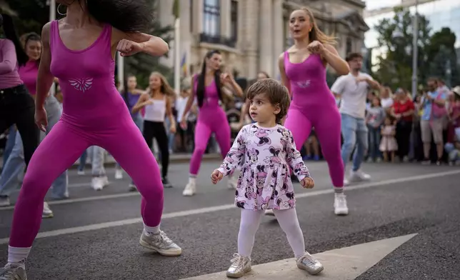 A child watches dancers perform outside the National History Museum of Romania during Dance Night, an event featuring a wide variety of dance styles performed on the Calea Victoriei avenue in Bucharest, Romania, Saturday, Aug. 23, 2025. (AP Photo/Andreea Alexandru)