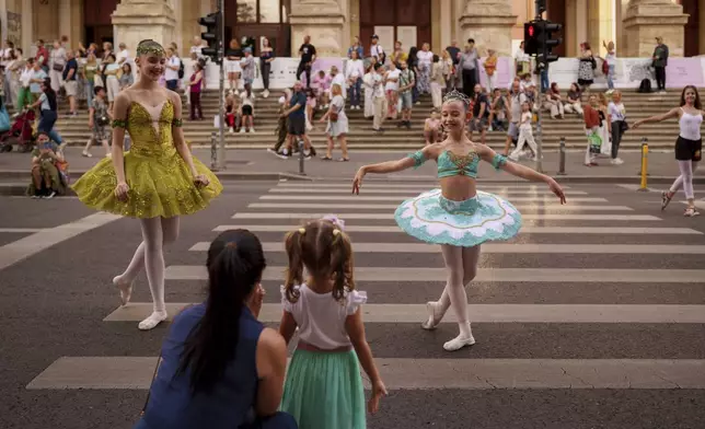 Daria Toma, 15, left, and Dora, 10, of the Romanian National Opera's Ballet Studio show dance moves for a little girl outside the National History Museum of Romania during Dance Night, an event featuring a wide variety of dance styles performed on the Calea Victoriei avenue in Bucharest, Romania, Saturday, Aug. 23, 2025. (AP Photo/Andreea Alexandru)