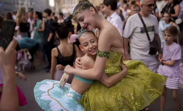 Daria Toma, 15, right, and Dora, 10, of the Romanian National Opera's Ballet Studio, hug outside the National History Museum of Romania during Dance Night, an event featuring a wide variety of dance styles performed on the Calea Victoriei avenue in Bucharest, Romania, Saturday, Aug. 23, 2025. (AP Photo/Andreea Alexandru)