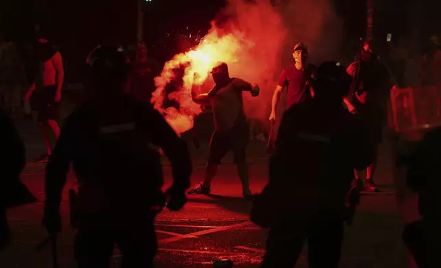 Supporters of Serbian President Aleksandar Vucic hurl flares at anti-government protesters during an anti-government protest in front of the Serbian Progressive Party office in Belgrade, Serbia, Thursday, Aug. 14, 2025. (AP Photo/Darko Vojinovic)