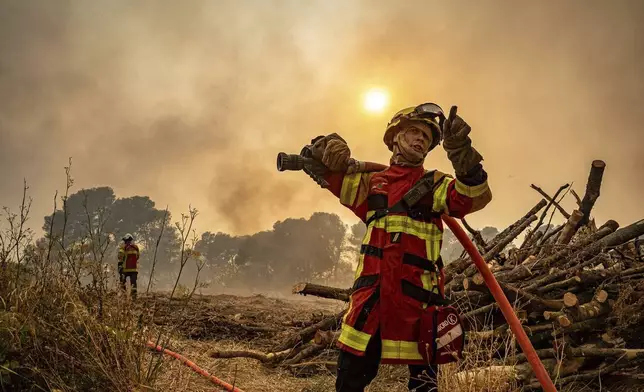 This photo, provided by the Securite Civile on Thursday Aug. 7, 2025, shows a fire man using a hose next to the wildfire near Saint-Laurent-de-la-Cabrerisse, southern France, Wednesday, Aug. 6, 2025. (Securite Civile via AP)