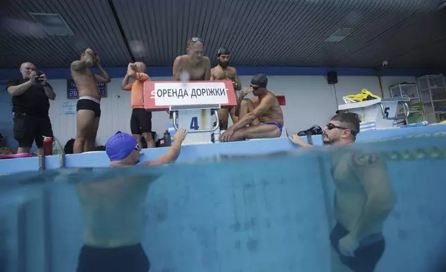Coach Roman Korol, center, instructs Ukrainian war veteran Oleksandr Dashko, right, at a pool in Kyiv, Ukraine, Tuesday, Aug. 12, 2025, during a training session for the upcoming 6.5km swimming race across the Bosporus Strait, (AP Photo/Evgeniy Maloletka)