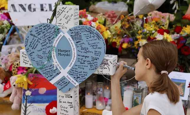 A child writes a message as people visit a make-shift memorial at Annunciation Catholic Church after the Wednesday's shooting at the school, Friday, Aug. 29, 2025, in Minneapolis. (AP Photo/Bruce Kluckhohn)