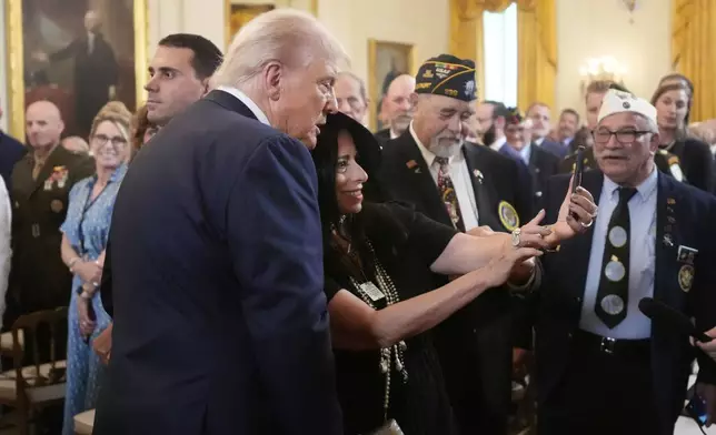 President Donald Trump, left, takes a selfie with an attendee as he departs an event to mark National Purple Heart Day in the East Room of the White House, Thursday, Aug. 7, 2025, in Washington. (AP Photo/Mark Schiefelbein)