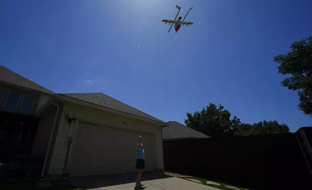 Julep Toth, 9, waves at a drone as it arrives at her house with a delivery, Thursday, July 31, 2025, in Frisco, Texas. (AP Photo/Julio Cortez)