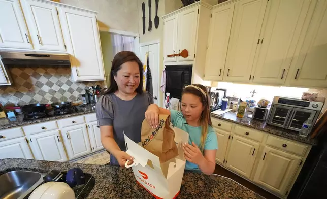 Janet Toth, left, and her daughter, Julep Toth, 9, open a delivery package after ordering a sandwich to their home Thursday, July 31, 2025, in Frisco, Texas. (AP Photo/Julio Cortez)