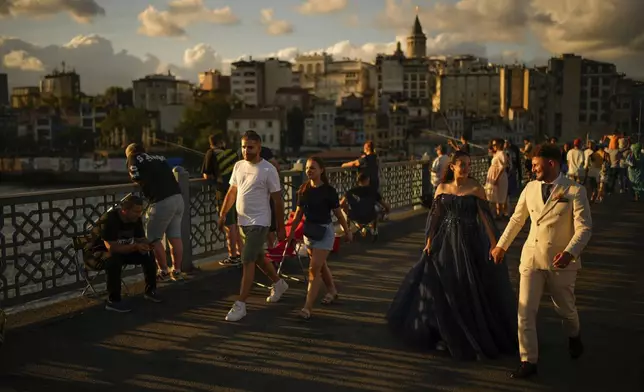 A couple wearing their wedding outfits walk along Galata bridge during a photo session, in Istanbul, Turkey, Thursday, July 31, 2025. (AP Photo/Emrah Gurel)