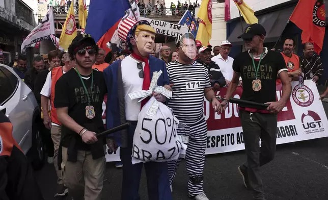 Protesters dressed as police escorting U.S. President Donald Trump and former president of Brazil Jair Bolsonaro demonstrate against Trump's announcement of 50% tariffs on Brazilian goods and against U.S. report that cited counterfeit product sales in Brazil, in Sao Paulo, Friday, July 18, 2025. (AP Photo/Ettore Chiereguini)