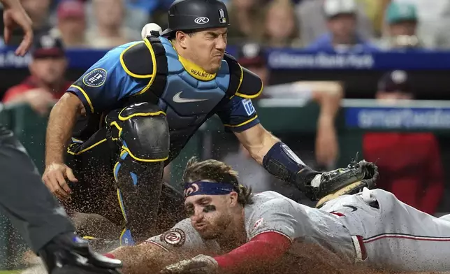Washington Nationals' Dylan Crews, bottom, scores past Philadelphia Phillies catcher J.T. Realmuto on a single by Daylen Lile during the ninth inning of a baseball game Friday, Aug. 22, 2025, in Philadelphia. (AP Photo/Matt Slocum)