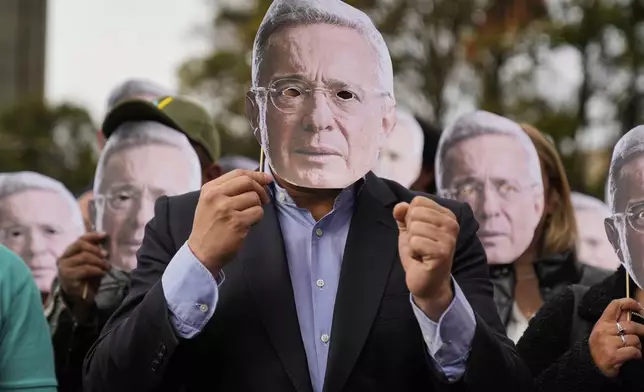 FILE - Supporters of former Colombian President Alvaro Uribe hold cutouts of his face outside the court where he was found guilty of witness tampering and bribery, in Bogota, Colombia, July 28, 2025. (AP Photo/Fernando Vergara, File)