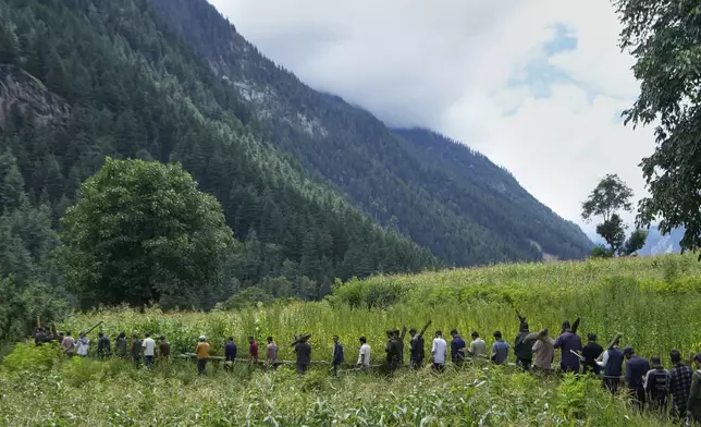 Villagers walk across a field carrying wood for mass cremation of people who died during Thursday's flash flood in Chositi village, Kishtwar district, Indian-controlled Kashmir, Friday, Aug. 15, 2025. (AP Photo/Channi Anand)