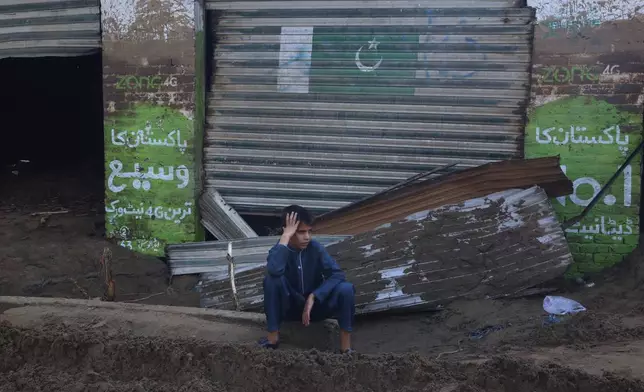 A boy sits in front of shops damaged by Friday's flash flooding on the outskirts of Pir Baba, Buner district, in Pakistan's northwest, Saturday, Aug. 16, 2025. (AP Photo/Muhammad Sajjad)
