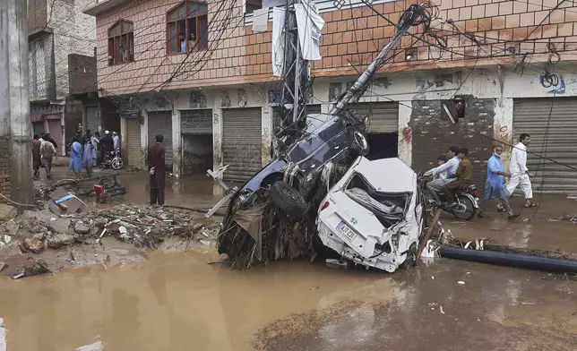 Local residents walk next to damaged cars stuck with an electric pole following flash flooding due to heavy rains at a neighbourhood of Mingora, the main town of Swat Valley, northwestern Pakistan, Friday, Aug. 15, 2025. (AP Photo/Naveed Ali)