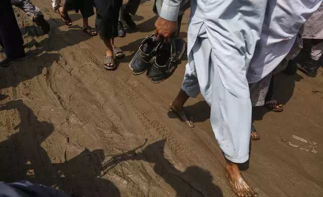 Local residents walk through a street covered with mud after Friday's flash flooding on the outskirts of Pir Baba, Buner district, in Pakistan's northwest, Saturday, Aug. 16, 2025. (AP Photo/Muhammad Sajjad)