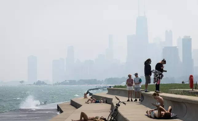 People sun tan on the Lakefront Trail on the North Side as a haze of Canadian wildfire smoke blankets the Chicago area and creates poor air quality, Thursday, July 31, 2025. (Ashlee Rezin/Chicago Sun-Times via AP)