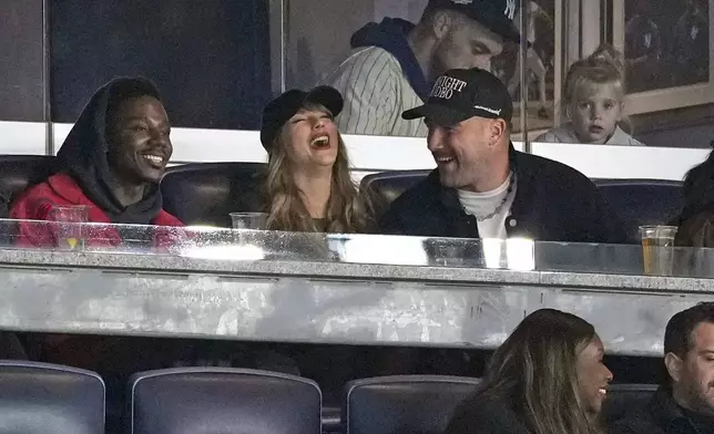 FILE - Travis Kelce, right, and Taylor Swift appear with actor-comedian Jerrod Carmichael, left, at Game 1 of the baseball AL Championship Series between the Cleveland Guardians and New York Yankees, Oct. 14, 2024, in New York. (AP Photo/Seth Wenig, File)