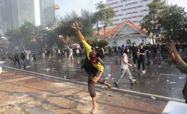 A man throws a rock at the police during a protest following the death of a delivery rider in clashes between riot police and students protesting against lawmakers' allowances, in Surabaya, East Java, Indonesia, Friday, Aug. 29, 2025. (AP Photo/Trisnadi)