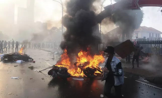 A man walks past burning motorcycles during a protest following the death of a delivery rider in clashes between riot police and students protesting against lawmakers' allowances, in Surabaya, East Java, Indonesia, Friday, Aug. 29, 2025. (AP Photo/Trisnadi)