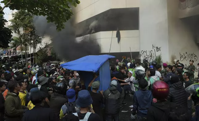 People gather near a burning building during a protest following the death of a delivery rider in clashes between riot police and students protesting against lawmakers' allowances, in Jakarta, Indonesia, Friday, Aug. 29, 2025. (AP Photo/Achmad Ibrahim)