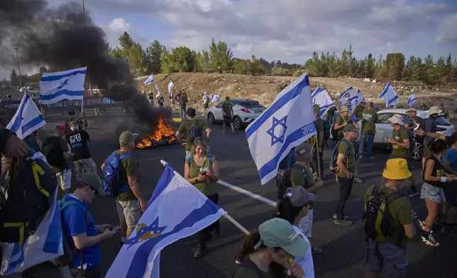 Demonstrators block a road during a protest demanding the immediate release of hostages held by Hamas and calling for the Israeli government to reverse its decision to take over Gaza City and other areas in the Gaza Strip, near Jerusalem, Israel, Sunday, Aug. 17, 2025. (AP Photo/Ohad Zwigenberg)