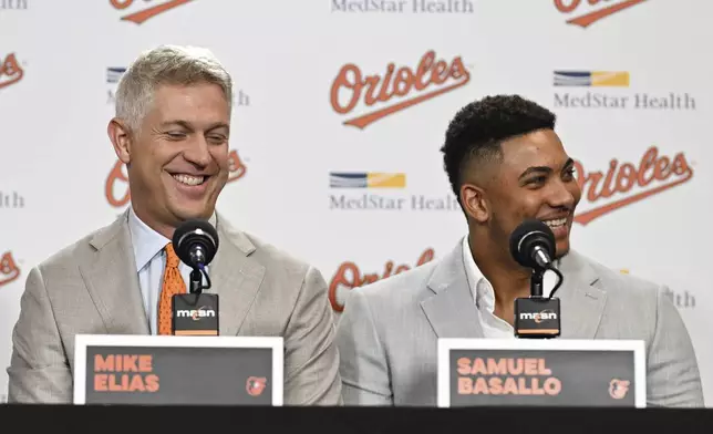 Baltimore Orioles executive vice president and general manager Mike Elias, left, and rookie catcher Samuel Basallo, right, share a laugh during a press conference after Basallo's signing of a contract extension Saturday, Aug. 23, 2025, in Baltimore. (AP Photo/Terrance Williams)
