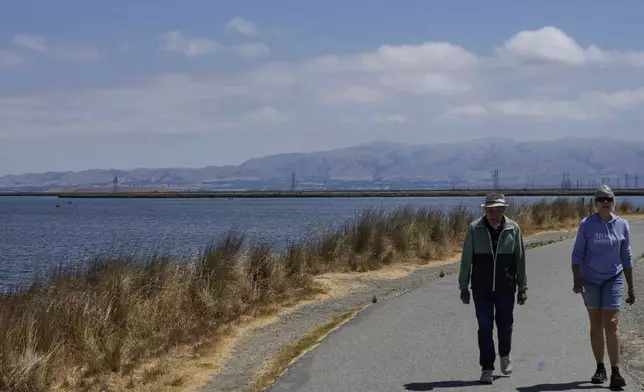 People walk on a trail next to Pond A1 in Mountain View, Calif., Thursday, July 24, 2025. (AP Photo/Godofredo A. Vásquez)