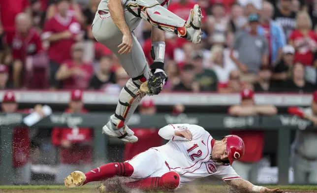 Cincinnati Reds' Austin Hays slides safe at home under leaping Philadelphia Phillies catcher J.T. Realmuto on a single hit by Noelvi Marte during the sixth inning of a baseball game Wednesday, Aug. 13, 2025, in Cincinnati. (AP Photo/Carolyn Kaster)