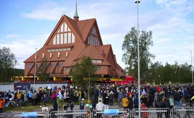 People gather outside the Kiruna Church, a Sami style wooden Swedish Lutheran church, called Kiruna Kyrka in Swedish, in Kiruna, Sweden, Tuesday, Aug. 19, 2025, as it is being moved along a 5-kilometer (3-mile) route east to a new city center as part of the town's relocation. (AP Photo/Malin Haarala)