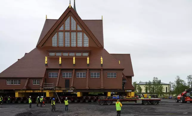 Construction workers and media stand near the Kiruna Church, a Sami style wooden Swedish Lutheran church, called Kiruna Kyrka in Swedish, in Kiruna, Sweden, Monday, Aug. 18, 2025, a day before it will be moved along a 5-kilometer (3-mile) route east to a new city center as part of the town's relocation.(AP Photo/Malin Haarala)