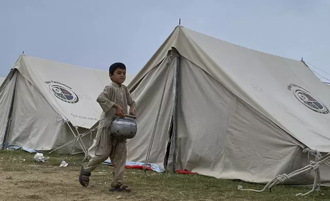 A boy, who fled his home with his family members after security forces launched a targeted operation against militants, walks carrying drinking water at a camp set up in a sports complex at Khar, in the Bajaur district of Khyber Pakhtunkhwa province bordering Afghanistan, Thursday, Aug. 14, 2025. (AP Photo/Qyass Khan)