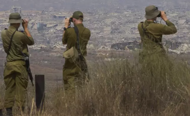 Israeli soldiers uses binoculars to look at damaged buildings in the Gaza Strip, from southern Israel, Wednesday, Aug. 13, 2025. (AP Photo/Ariel Schalit)