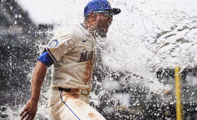 Seattle Mariners' Julio Rodriguez reacts while being doused by teammate Victor Robles to celebrate a win over the Texas Rangers in a baseball game Sunday, Aug. 3, 2025, in Seattle. (AP Photo/Lindsey Wasson)