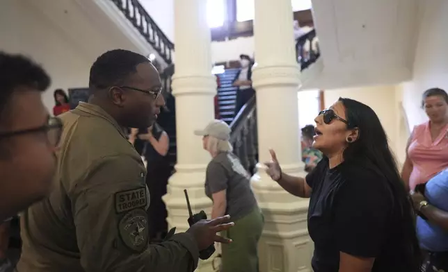 A Texas state trooper engages with a protester over noise volume outside of the House Chamber where Democratic Texas Rep. Nicole Collier refuses to leave due to a required law enforcement escort, Tuesday, Aug. 19, 2025, in Austin, Texas. (AP Photo/Eric Gay)