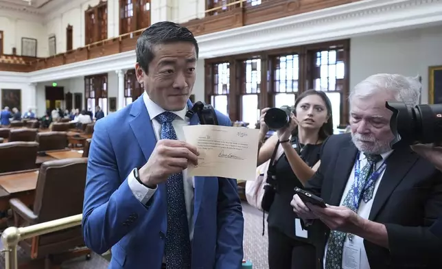 Texas state Rep. Gene Wu, left, shows members of the media his permission slip to leave the House Chamber, Monday, Aug. 18, 2025, in Austin, Texas. (AP Photo/Eric Gay)