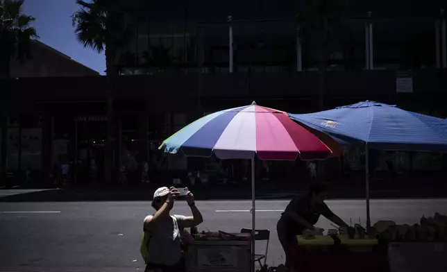A visitor takes pictures of the TCL Chinese Theatre as a street vendor works nearby in the Hollywood section of Los Angeles, Tuesday, Aug. 19, 2025. (AP Photo/Jae C. Hong)