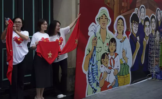 Women take picture with Vietnam's national flag as the nation celebrating Vietnam's 80th National Day in Hanoi, Friday, Aug. 29, 2025. (AP Photo/Vincent Thian)