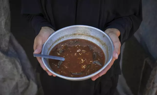 Palestinian woman Sally Muzhed, 38, displaced from Deir al-Balah, poses for a picture holding a plate with eggplant, her only food for the day, amid severe food shortages in the Gaza Strip, in Deir al-Balah, Monday, Aug. 4, 2025. (AP Photo/Abdel Kareem Hana)