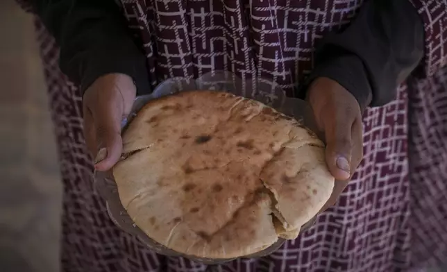 Palestinian woman Heba Al-Mubayed, displaced from Khan Yunis, poses for a picture holding a plate with a piece of bread, her only food for the day, amid severe food shortages in the Gaza Strip, in Khan Yunis, Monday, July 28, 2025. (AP Photo/Abdel Kareem Hana)